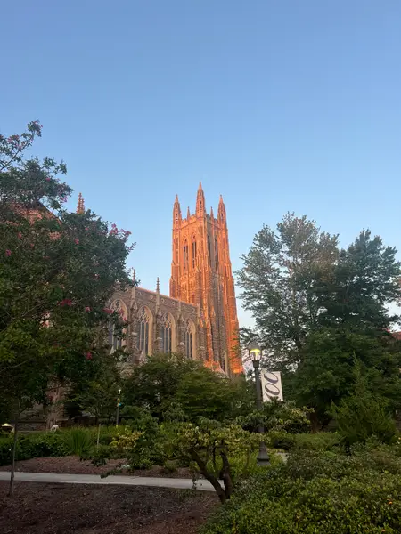 Duke Chapel tower lit orange at sunset above campus trees