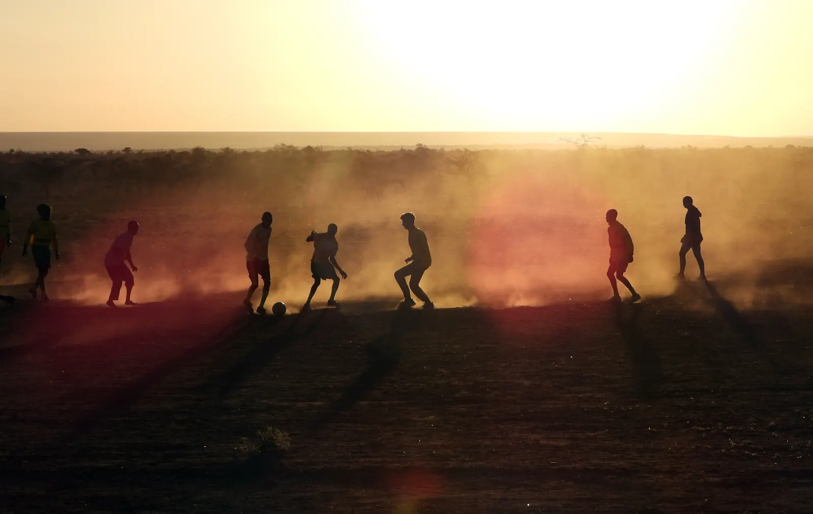Pickup soccer game at sunset, players silhouetted in red dust