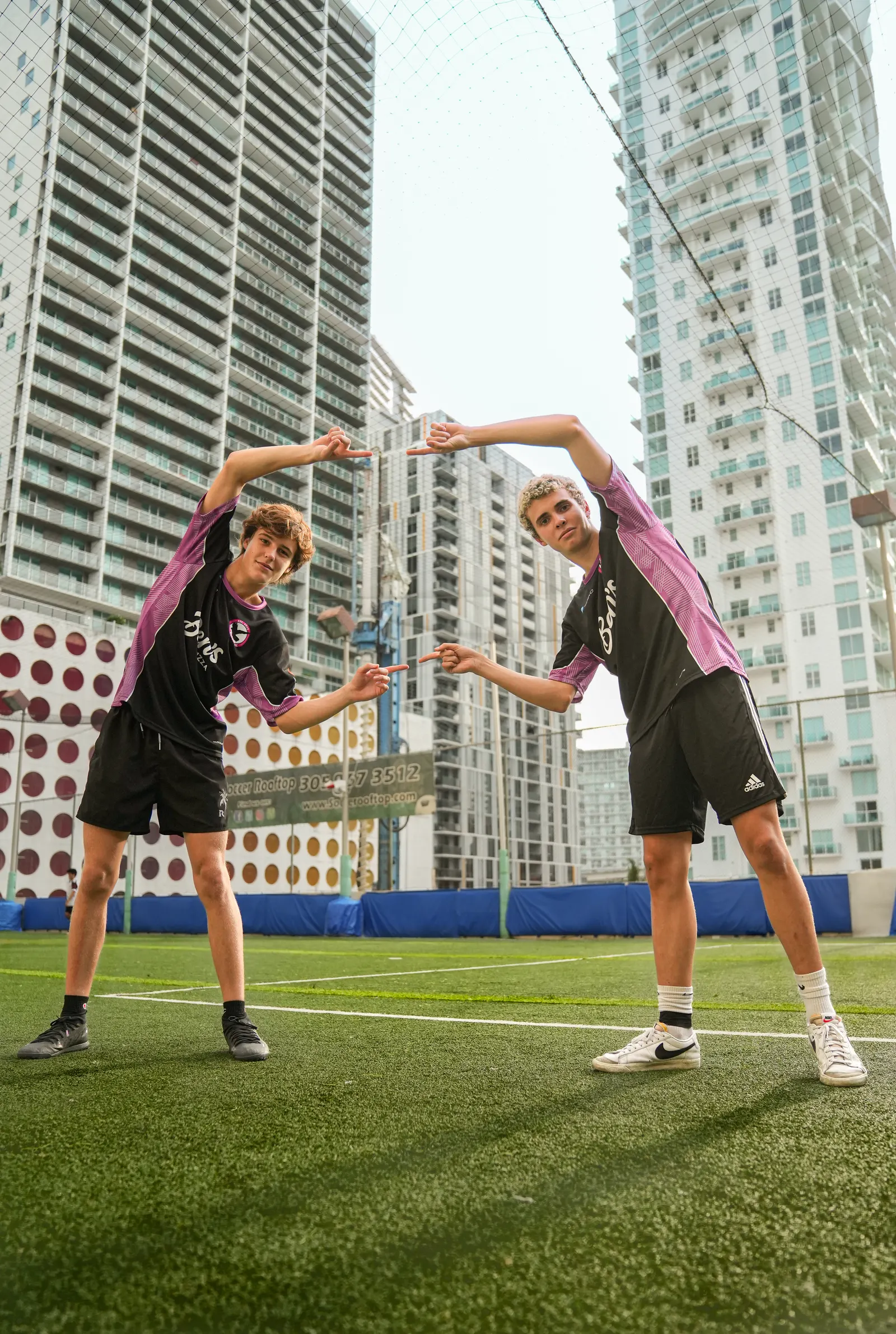Two soccer players in pink and black kits posing between city towers
