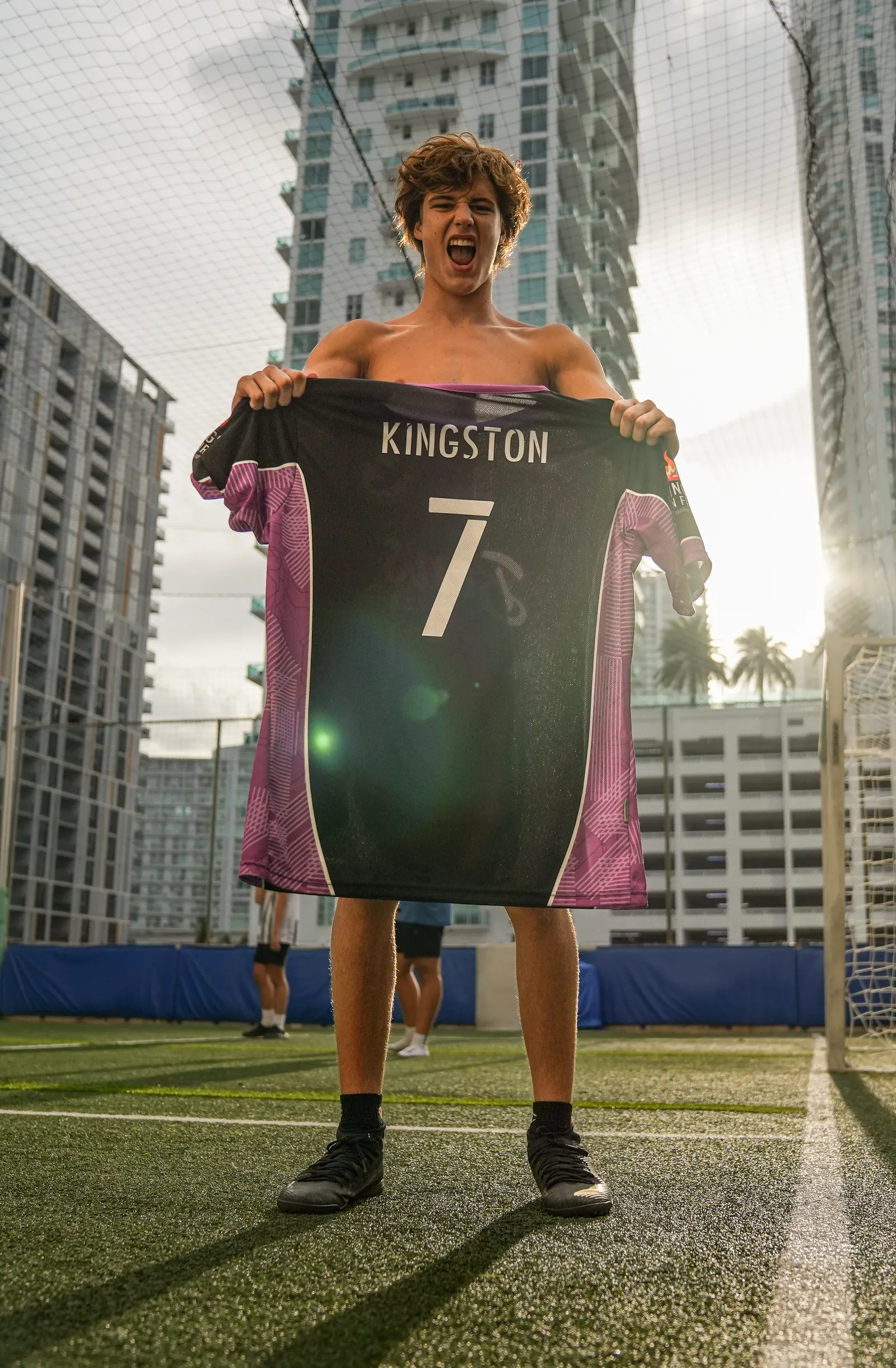 Player holding up a number 7 Kingston jersey on a rooftop pitch