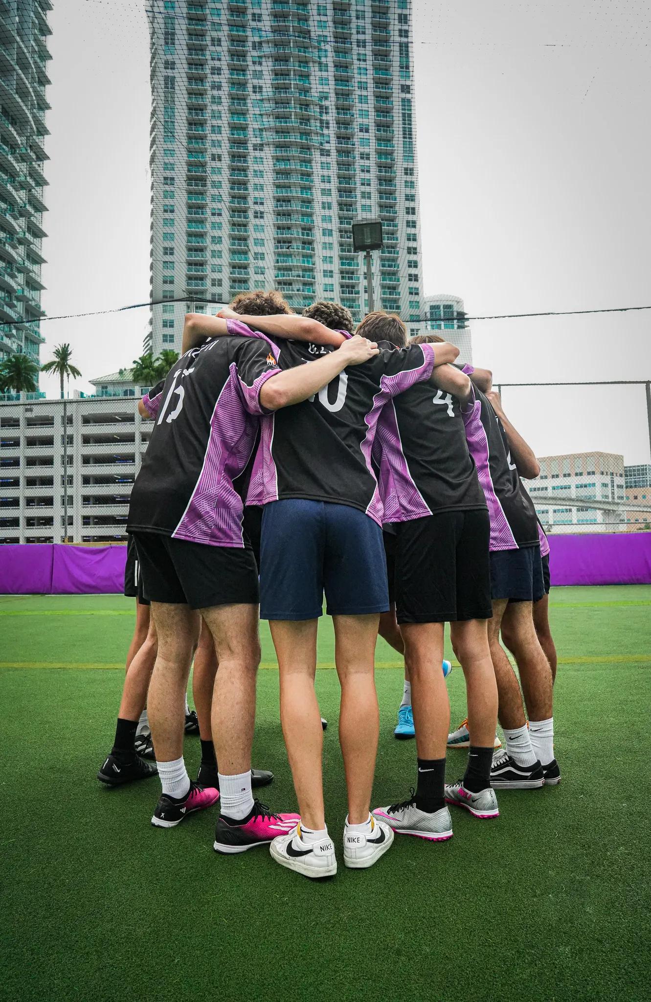 Team huddle on a turf pitch with a tower behind