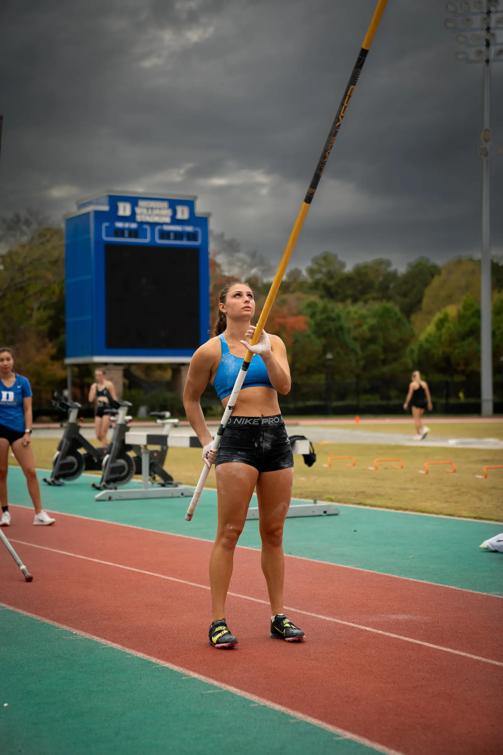Pole vaulter standing on the runway holding her pole upright