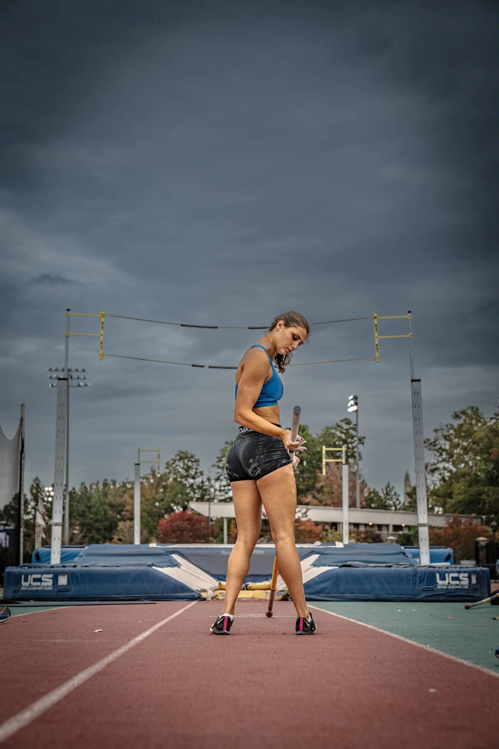 Pole vaulter walking down the runway under dark clouds