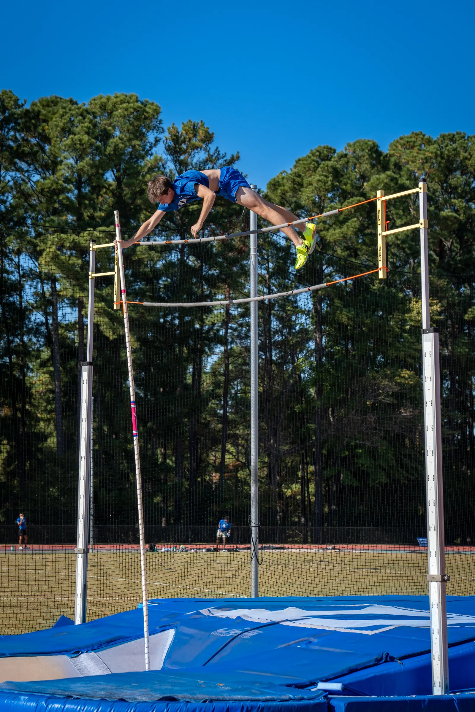 Pole vaulter clearing the bar against tall pines