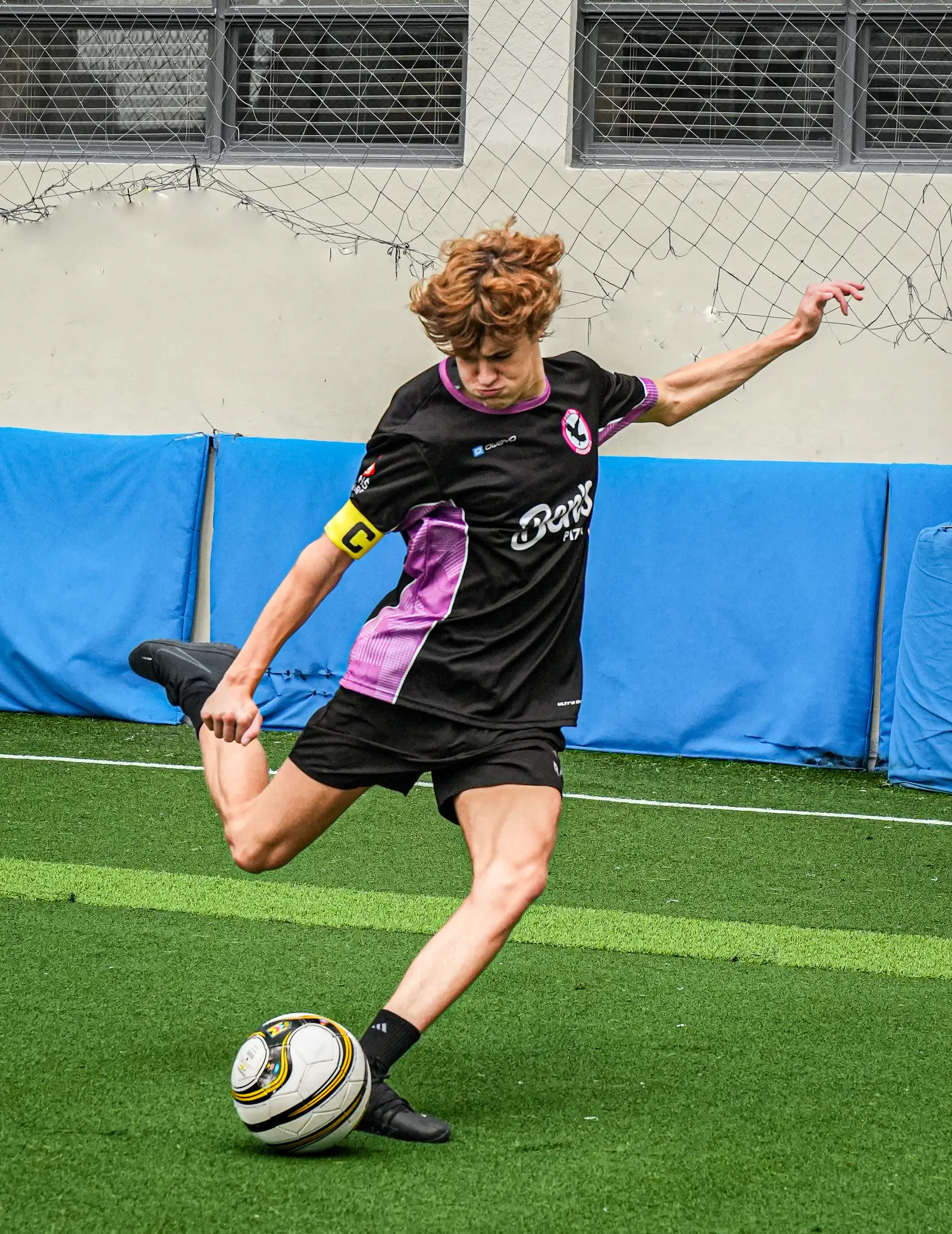 Player in a pink and black kit about to strike a soccer ball