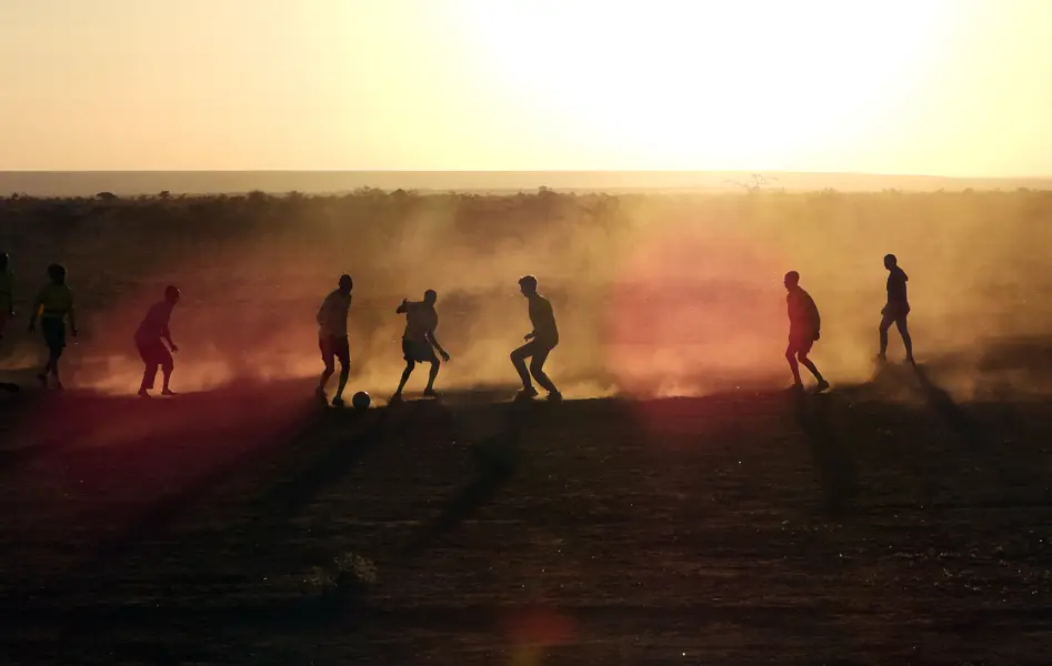 Pickup soccer game at sunset, players silhouetted in red dust